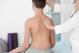 Healthcare provider examining a child’s back and shoulder alignment during a scoliosis evaluation.